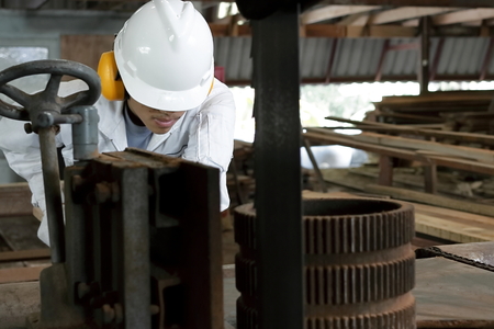Close up young worker in uniform with safety equipment cutting a piece of wood on vertical band saw...