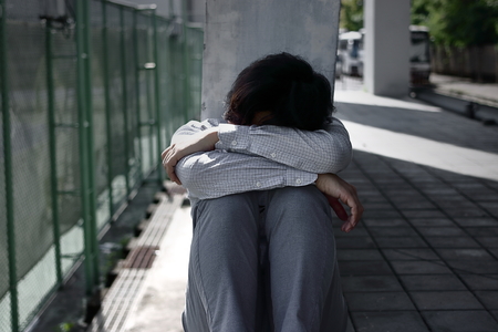 Frustrated exhausted young Asian business man sits and hugs his knees up to the chestの写真素材