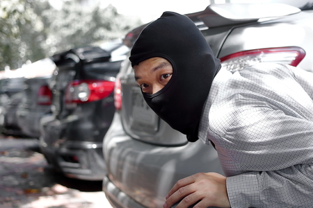 Masked burglar wearing a balaclava ready to burglary against car background. Insurance crime concept.の写真素材