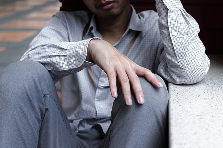 Selective focus on hands of Frustrated stressed young Asian business man sitting on the floorの写真素材
