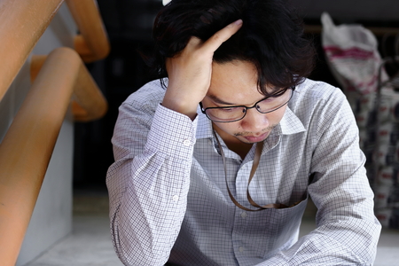 Portrait of frustrated stressed young Asian man touching head and feeling tried or exhausted.の写真素材