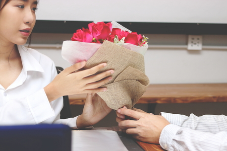 Cropped image of attractive young Asian woman accepting a bouquet of red roses from boyfriend in office on valentine's day. Love and romance in workplace concept.の写真素材