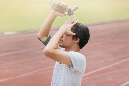 Healthy young Asian fitness man splashing water on his face after run in track of stadium. Sunshine effect.の写真素材