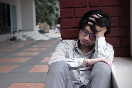 Frustrated stressed young Asian man touching head and feeling disappionted or exhausted. Unemployed businessman concept.の写真素材