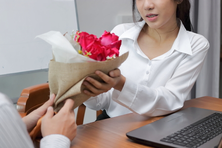 Cropped image of attractive young Asian woman accepting a bouquet of red roses from boyfriend in...
