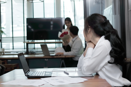 Envious angry Asian business woman looking affectionate couple in love in office. Jealousy and envy in friend relationshipの写真素材