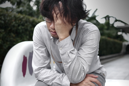 Front view of frustrated stressed young Asian business man with hands touching head and feeling...