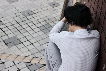 Back view of frustrated stressed young Asian employee man touching head and feeling disappointed or exhausted. Unemployed businessman concept.の写真素材
