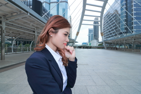 Wide angle shot of attractive young Asian business woman in suit thinking about her job at urban building background.の写真素材