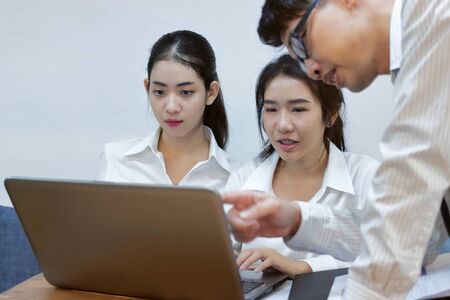 Young Asian business people working together on a laptop computer at office. Teamwork brainstroming concept. Selective focus and shallow depth of field.の写真素材