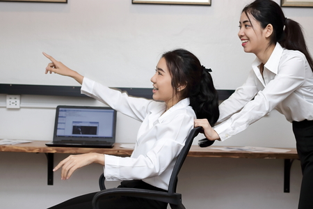 Cheerful young Asian business woman push chair and having fun together in office.