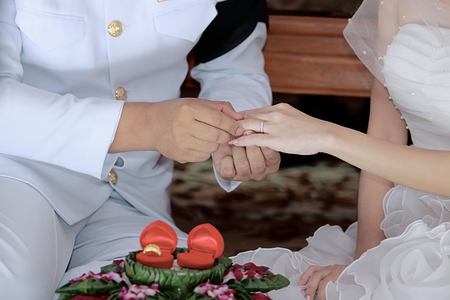 Groom newlyweds wearing ring on bride's finger in wedding ceremony.の写真素材