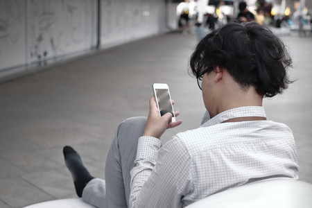 Frustrated anxious young Asian business man using mobile smart phone at outside officeの写真素材