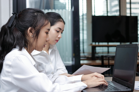 Two young Asian businesswoman working together on a laptop computer at office.の写真素材