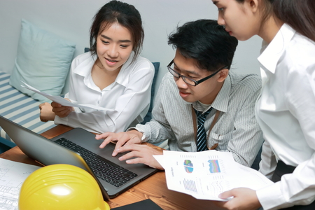 Group of young Asian business people working together on a laptop computer at office. Teamwork brainstroming concept. Selective focus and shallow depth of field.の写真素材