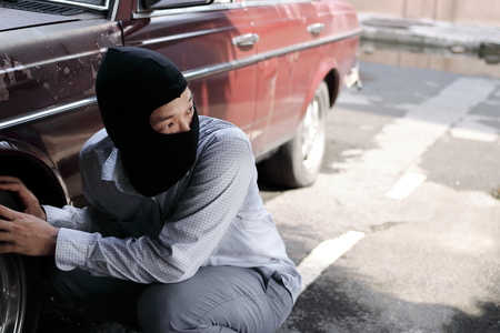Masked burglar wearing a balaclava ready to burglary against car background. Insurance crime concept.の写真素材