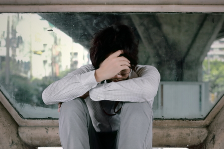 Anxious frustrated young Asian business man sitting and touching forehead with hands.の写真素材