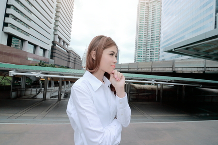 Wide angel shot of confident young Asian woman standing and thinking posing at urban building public background.の写真素材