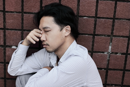 Anxious stressed young Asian business man suffering from severe depression. Thoughtful conceptの写真素材