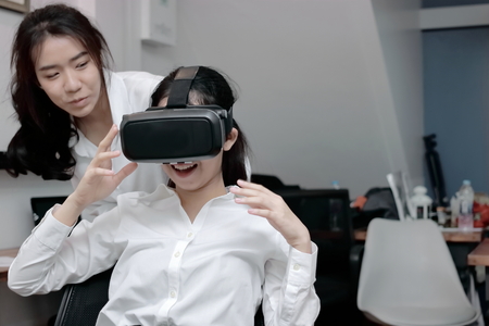 Attractive young Asian business woman wearing virtual VR reality glasses and having fun in office.の写真素材