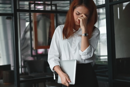 Upset stressed Asian business woman standing and feeling disappointed or tired in office.の写真素材