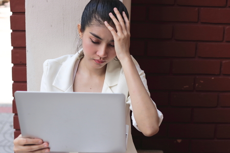 Tired overworked young Asian business woman with hands on head suffering from troubleの写真素材