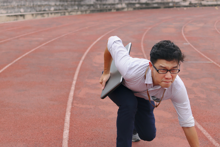 Confident young Asian business man with laptop ready start position to forward on race track.の写真素材
