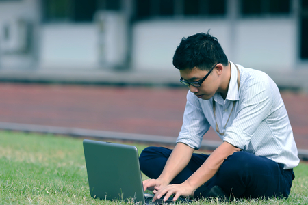 Vintage toned image of relaxed young Asian business man working with laptop on green grass.の写真素材