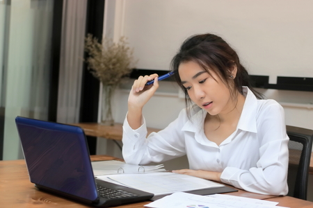 Portrait of attractive young Asian businesswoman working on the workplace in office. Thinking and thoughtful business concept.の写真素材