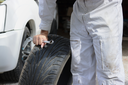 Professional young mechanic in uniform with spare tires and wrench for fixing car at the repair garage background.の写真素材