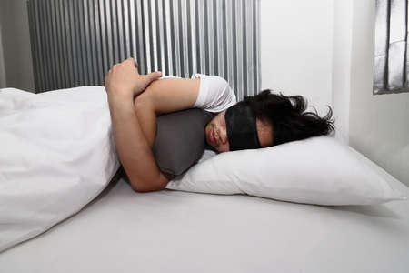 Young Asian man with mask comfortable sleeping on the bed in home.の写真素材