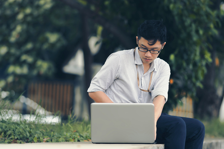 Vintage toned image of relaxed young Asian business man working with laptop at public park.の写真素材