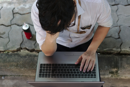 Top view of depressed young Asian business man sitting and using mobile smart phone and laptop.