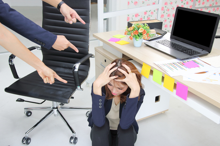 Anxious upset young Asian business woman with fingers pointing at her in workplace of office.の写真素材