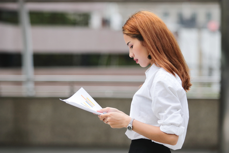 Side view of confident young Asian business woman analyzing charts or paperwork during walkingの写真素材