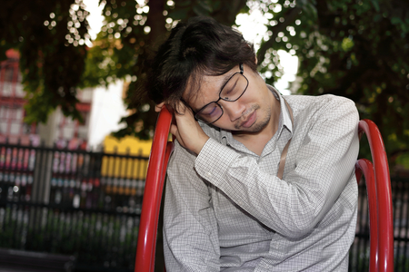Upset exhausted Asian man in depression sitting on playground slide