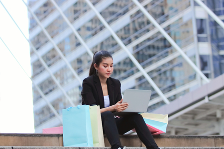 Attractive young Asian woman with colorful shopping bag sitting at outdoors.の写真素材