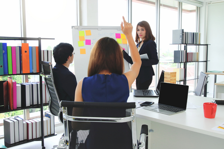 Back view of young Asian woman raising hands and asking a question during presentation in conference roomの写真素材