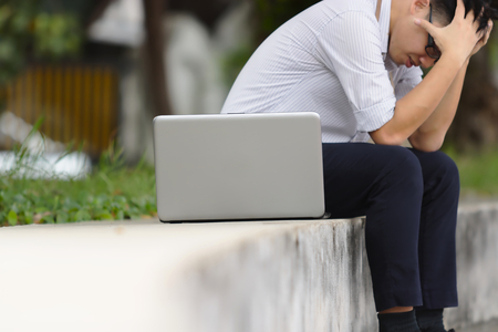 Selective focus on laptop with troubled stressed Asian business man covering face with handsの写真素材