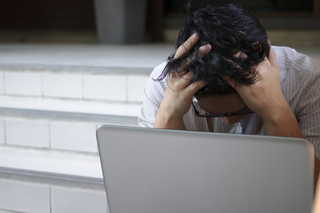 Frustrated upset young Asian business man covering face with hands in depressionの写真素材