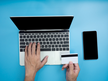Top view of hands on computer laptop and credit card on blue background. Internet and shopping...