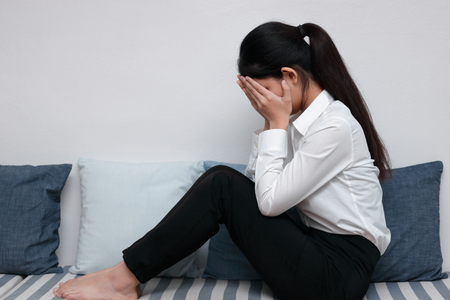 Side view of tired stressed young Asian woman covering face with hands in living room.の写真素材