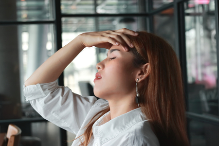 Confused upset young Asian business woman suffering from severe from depression in workplace.の写真素材