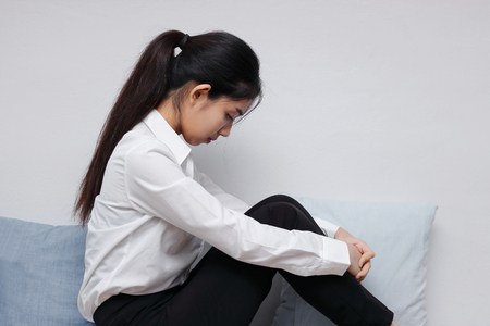 Side view of tired upset young Asian woman sitting in living room.の写真素材