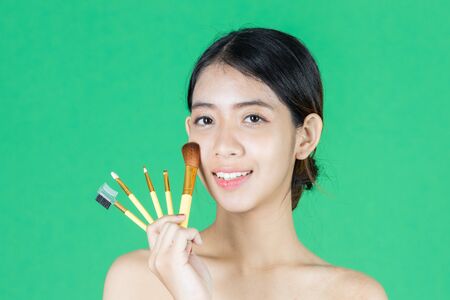 Beauty young Asian woman holding makeup brushes over green isolated background. Healthy and cosmetics concept.の写真素材