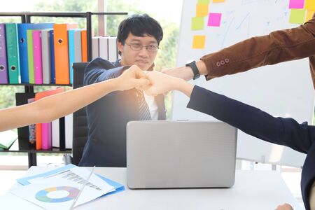 Hands of young business people giving fist bump together to greeting complete dealing in office with sunshine effect. Success and teamwork concept.の写真素材