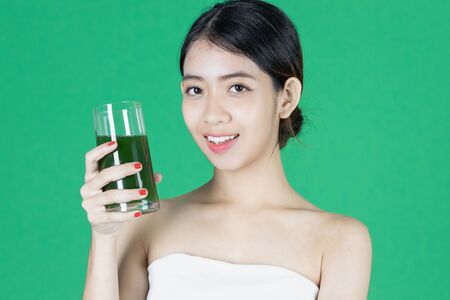 Attractive fresh young Asian woman drinking green vegetable detox drink over green isolated background. Healthy and lifestyle concept.の写真素材