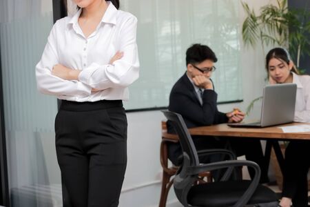 Leadership business woman concept. Cropped image of young Asian businesswoman standing against her colleague in office background.の写真素材