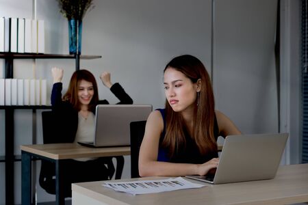 Angry envious Asian business woman looking successful competitor colleague in office. Low key toned imageの写真素材