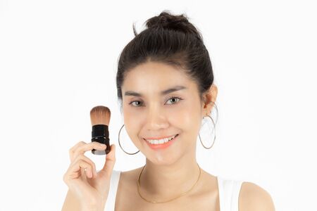 Beauty face of young Asian woman applying make up with brush over white isolated background. Healthy...
